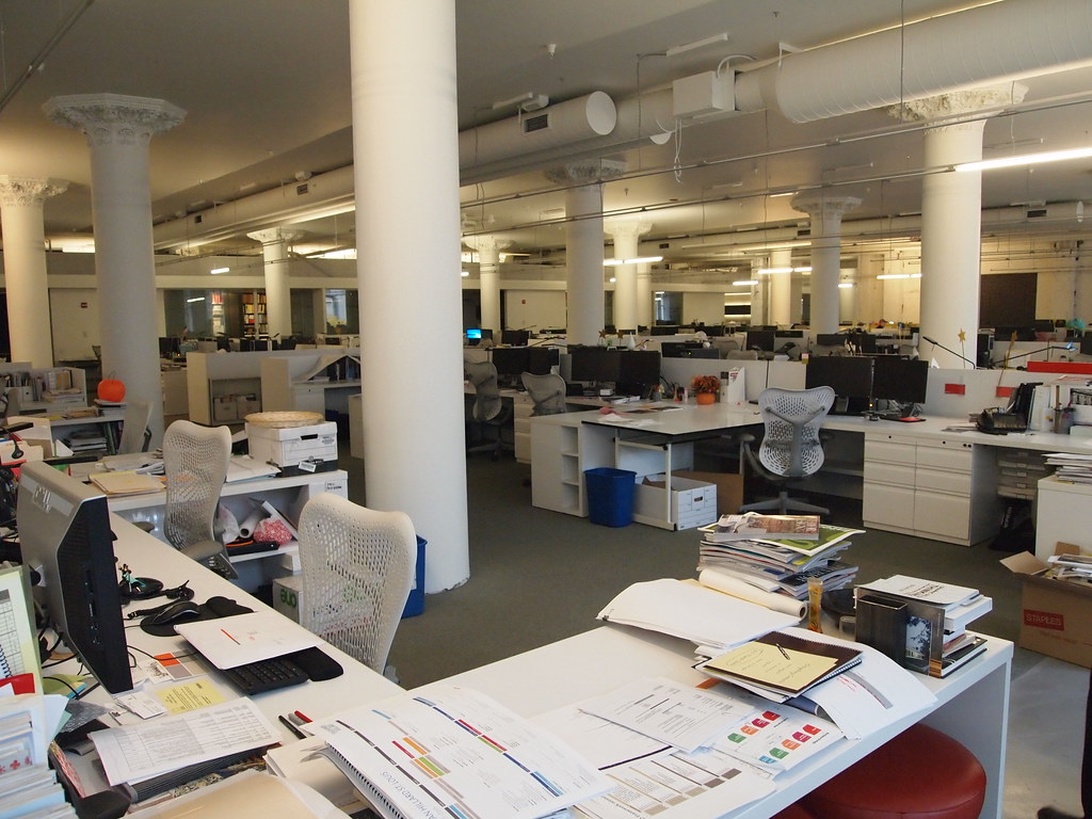 En stor öppen kontorsyta i en historisk byggnad med vita pelare och dekorativa kapitäl, där moderna arbetsstationer är integrerade med den klassiska arkitekturen.