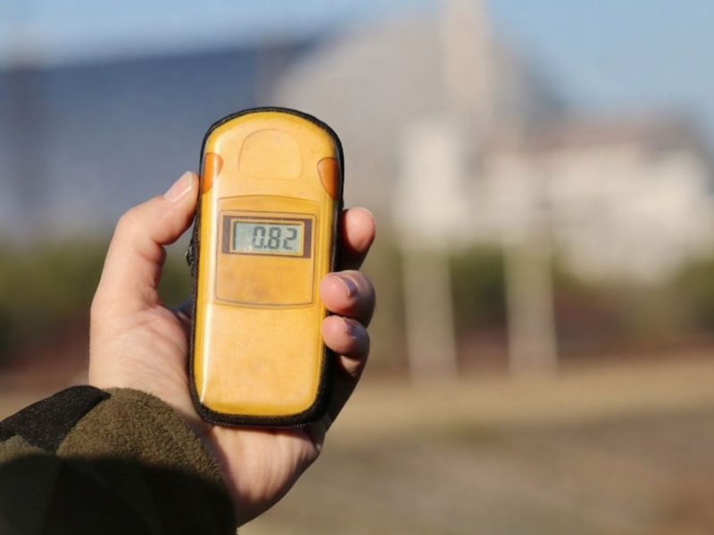 Hand håller en gul strålningsmätare med digital display som visar "0.82".