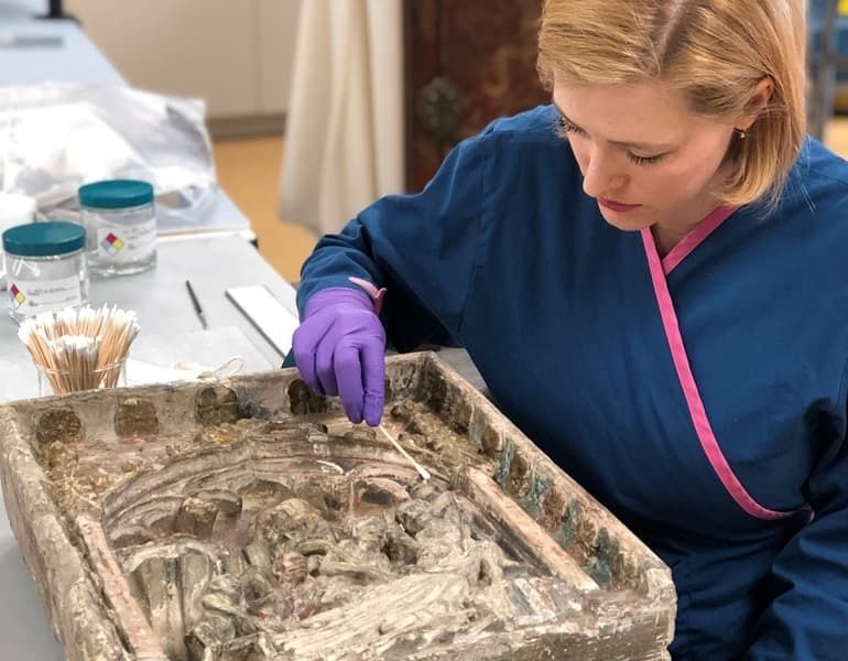 Konservator undersöker sköra textilfragment med pincett och handskar